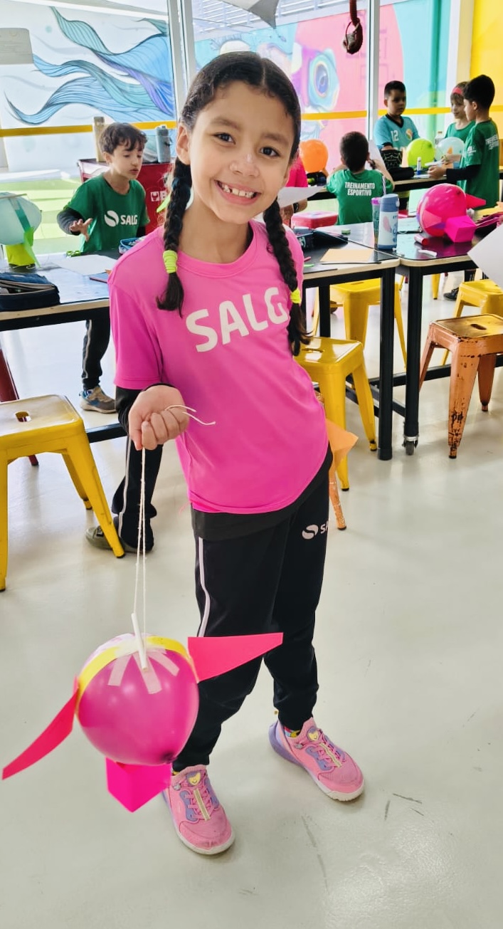Aluna segurando um foguete de bexiga rosa durante a atividade de Cultura e Inovação